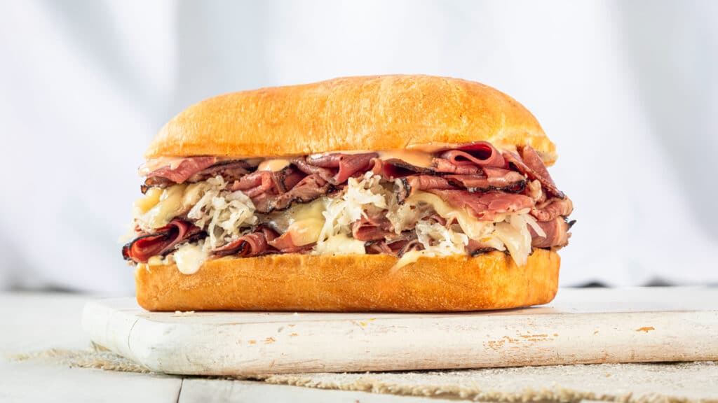 Earl of Sandwich pastrami sandwich with sliced pastrami, melted Swiss, sauerkraut, and dressing on a toasted roll.